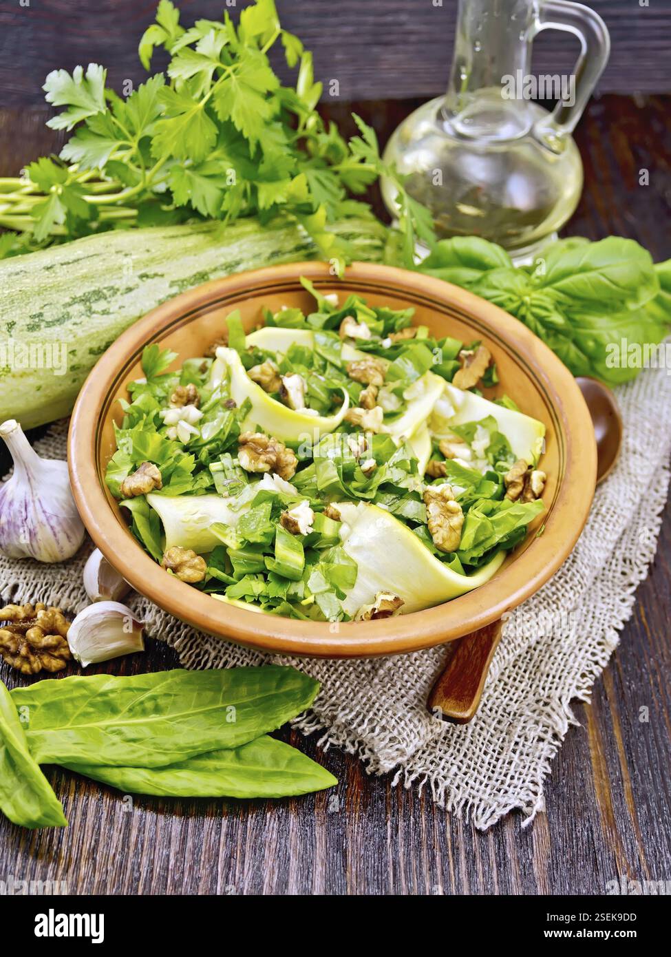 Salade de jeunes courgettes, de l'oseille, l'ail et les noix, assaisonnés d'huile végétale dans une assiette sur nappes de sacs sur fond de bois Banque D'Images