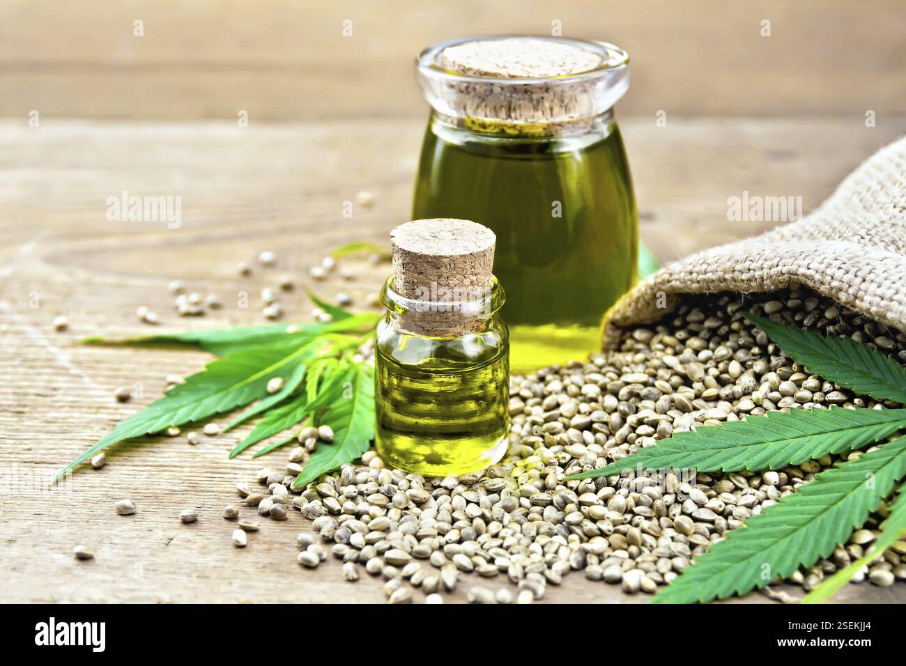 L'huile de chanvre dans deux pots en verre avec le grain dans le sac, les feuilles et les tiges du cannabis sur l'arrière-plan de vieux panneaux en bois Banque D'Images