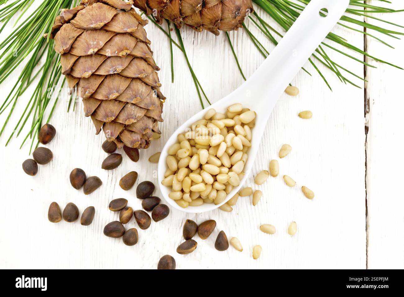 Pelées de noix de cèdre dans une cuillère, deux pommes de pin et des noix dans la coquille contre une planche en bois clair sur le dessus Banque D'Images