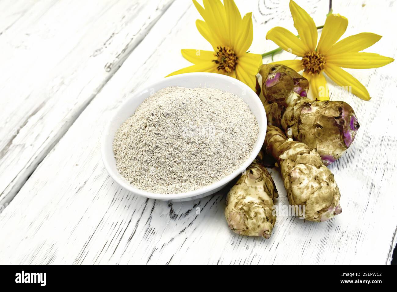 La farine de topinambours dans un bol blanc avec des fleurs jaunes et les légumes sur le fond de panneaux de bois Banque D'Images