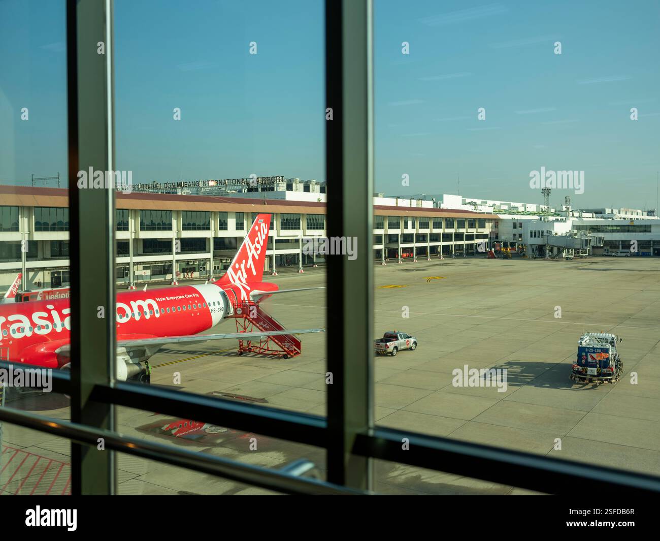 Avion Air Asia à l'aéroport de Don Mueang vu à travers de grandes fenêtres en verre à la porte d'embarquement par une journée ensoleillée. Banque D'Images