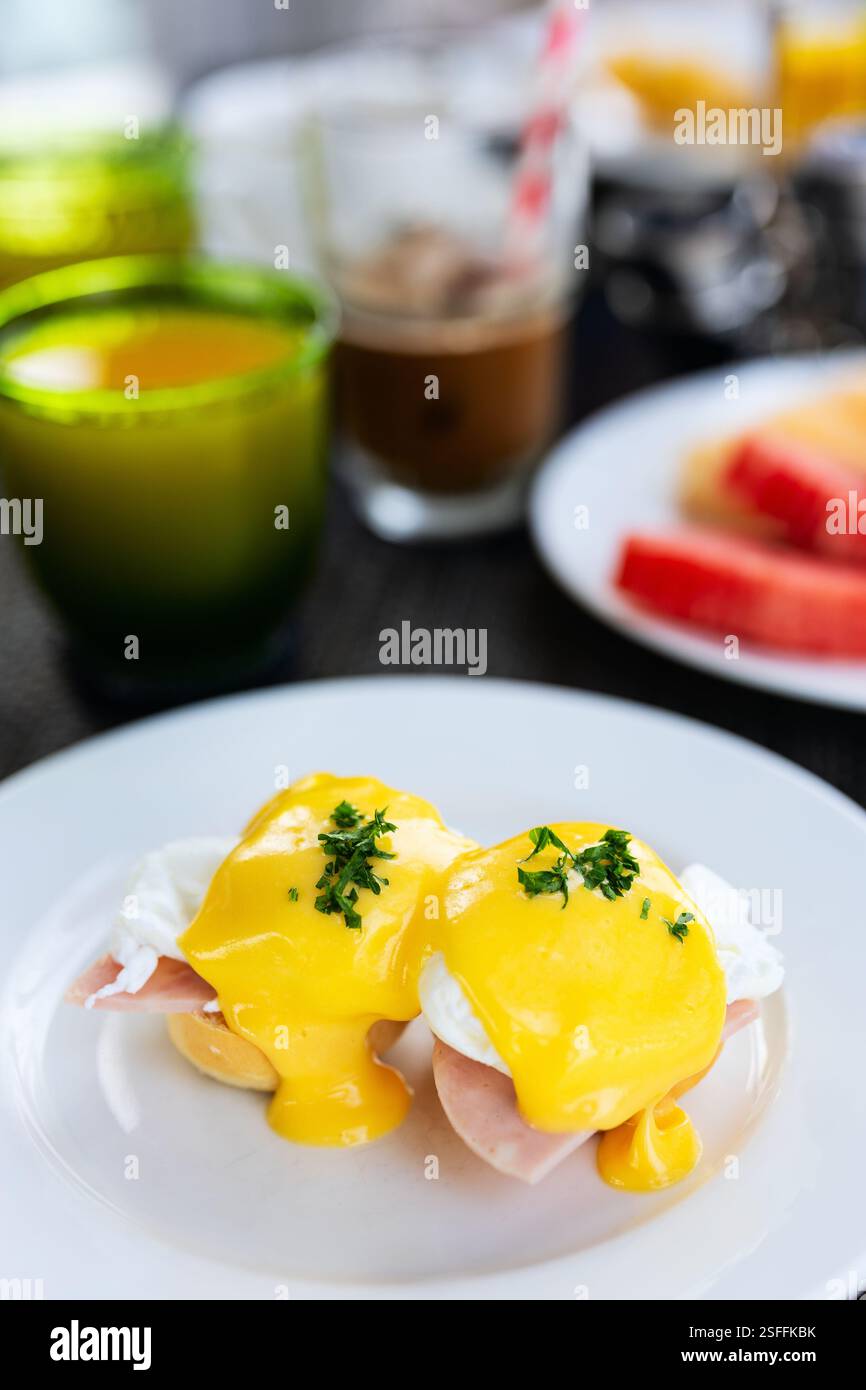 Gros plan de deux œufs Benoît sur une assiette blanche, recouverts d’une riche sauce hollandaise jaune et garnis de persil, servis à table du petit déjeuner Banque D'Images