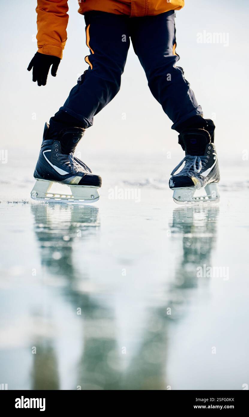 Homme athlète en veste jaune patin sur glace sur le lac gelé avec des fissures et de la neige à l'heure d'hiver. Gros plan de jambe de patin à glace Banque D'Images
