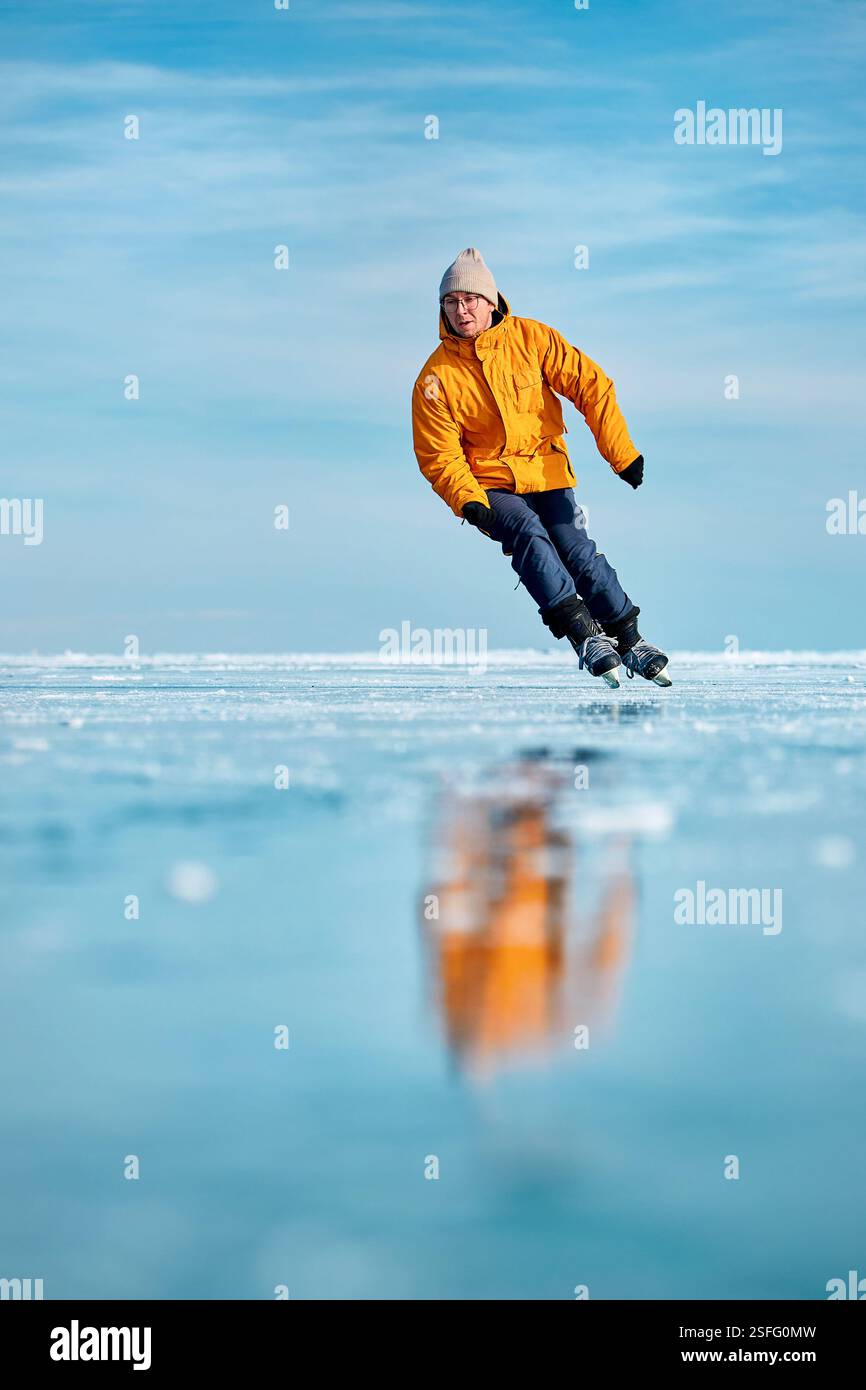 Homme athlète en veste jaune patin sur glace sur le lac gelé avec réflexion à l'heure d'hiver Banque D'Images