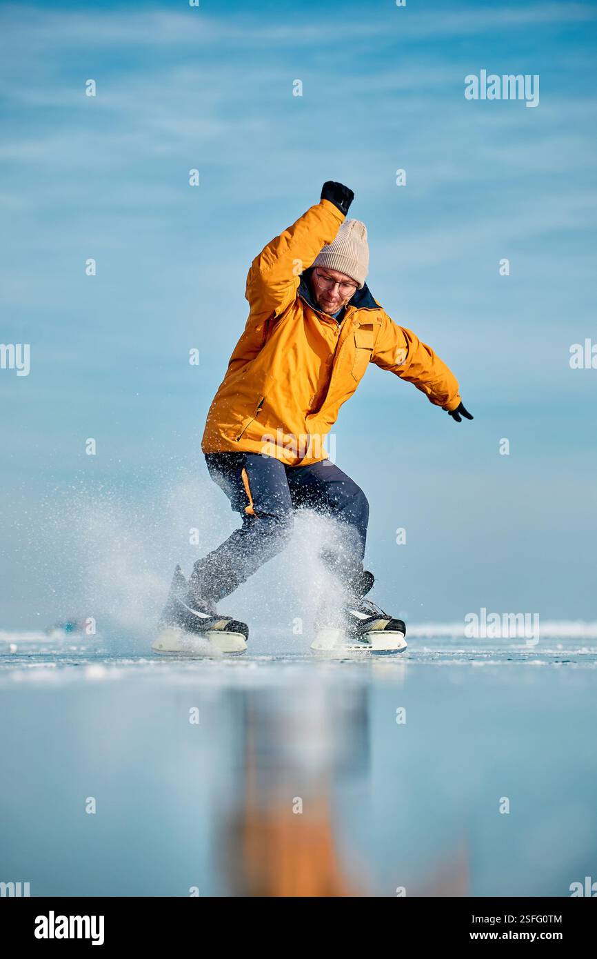 Homme athlète en veste jaune patin sur glace sur le lac gelé avec réflexion à l'heure d'hiver Banque D'Images