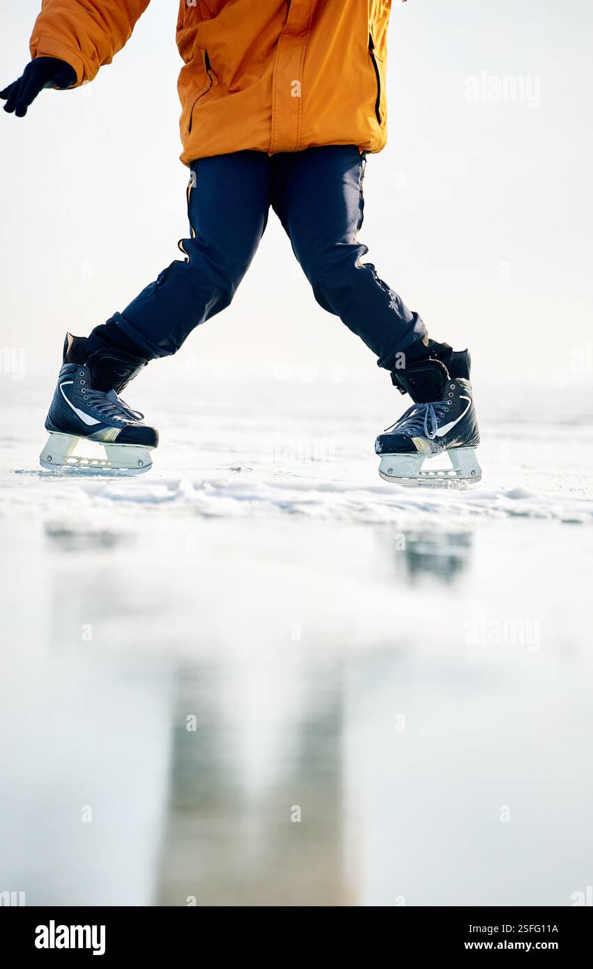 Homme athlète en veste jaune patin sur glace sur le lac gelé avec des fissures et de la neige à l'heure d'hiver. Gros plan de jambe de patin à glace Banque D'Images