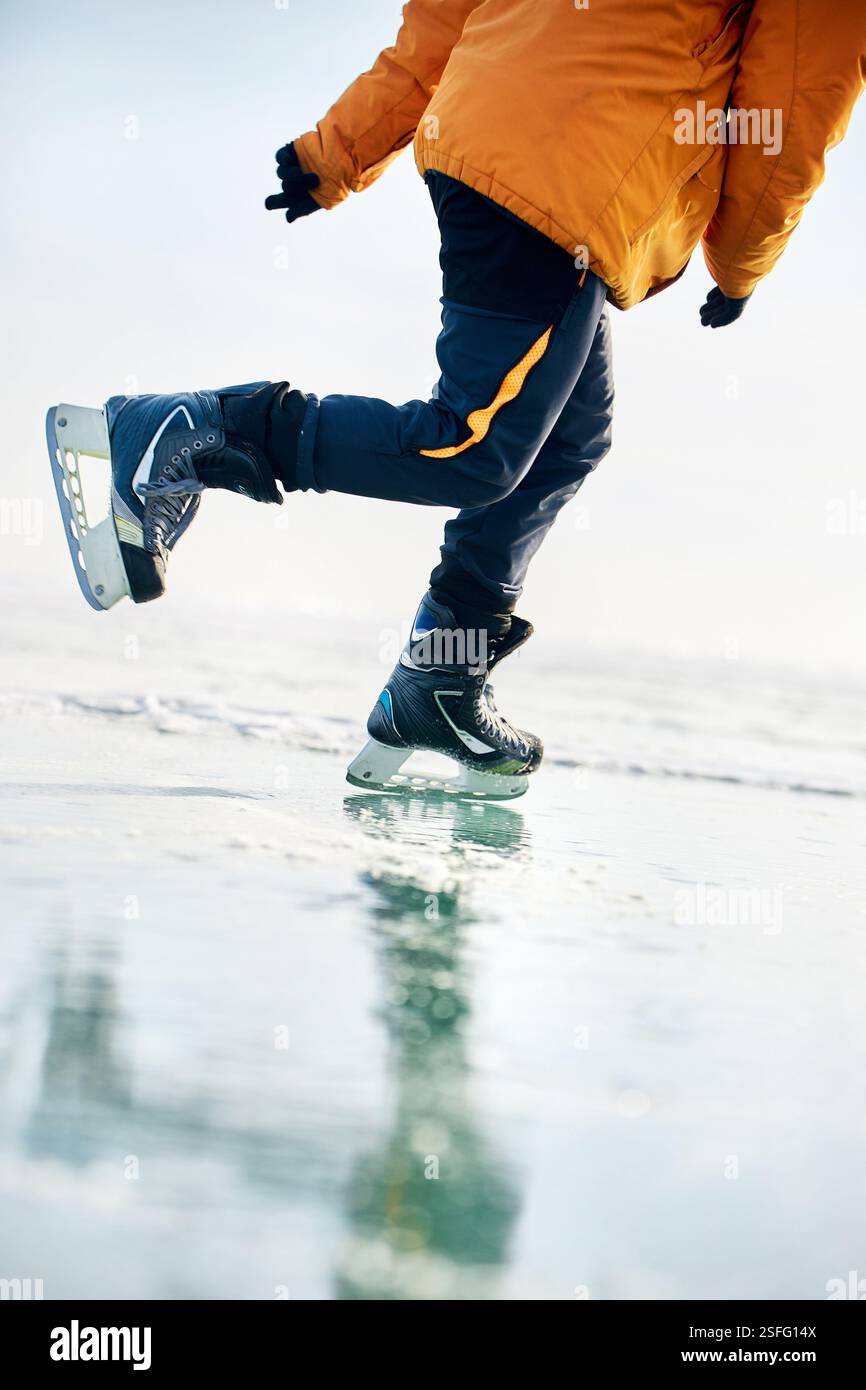 Homme athlète en veste jaune patin sur glace sur le lac gelé avec des fissures et de la neige à l'heure d'hiver. Gros plan de jambe de patin à glace Banque D'Images