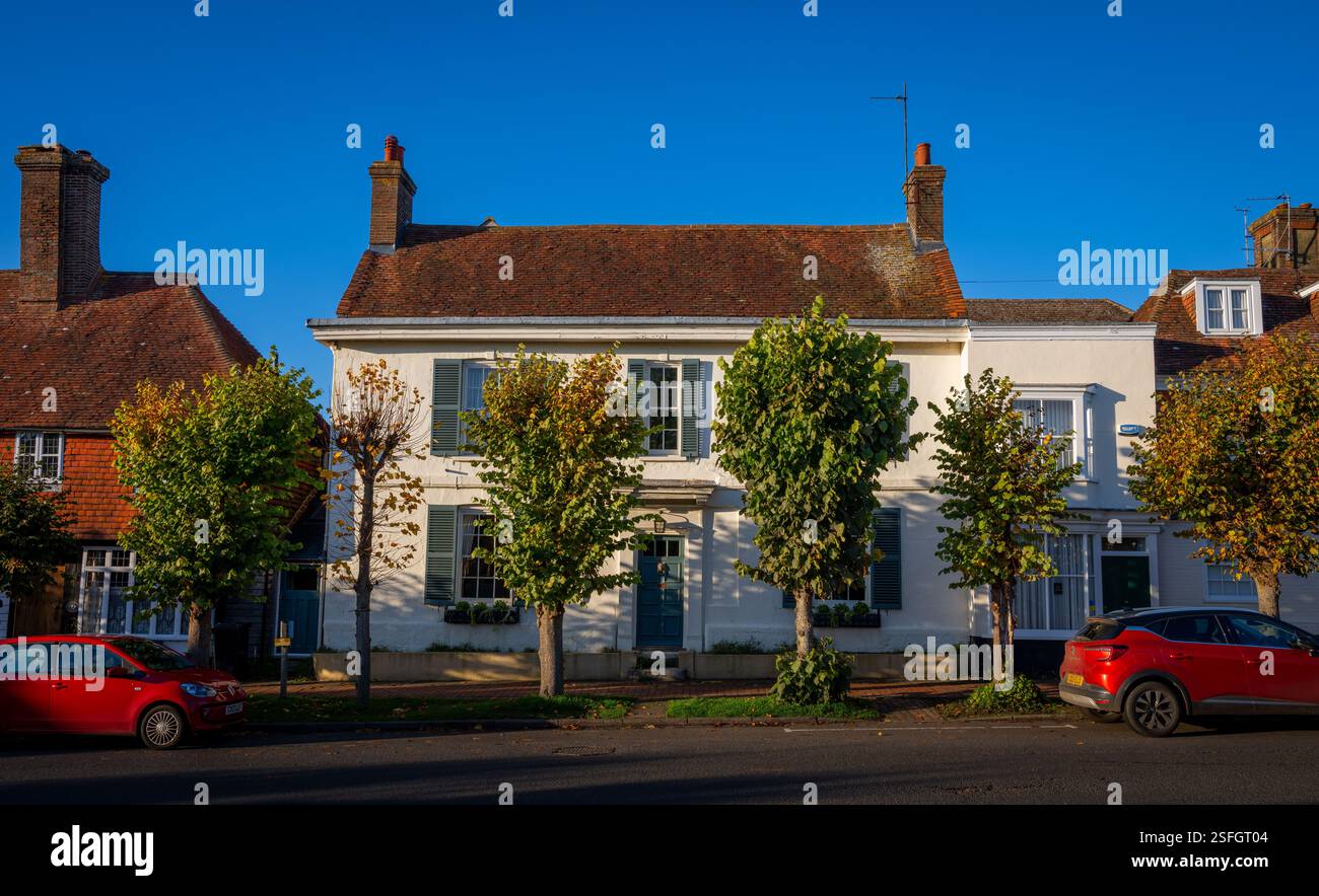 Burwash, East Sussex, Royaume-Uni : vieille maison sur Burwash High Street. Ce bâtiment traditionnel a des murs blancs et des volets verts. Des arbres bordent la route. Banque D'Images