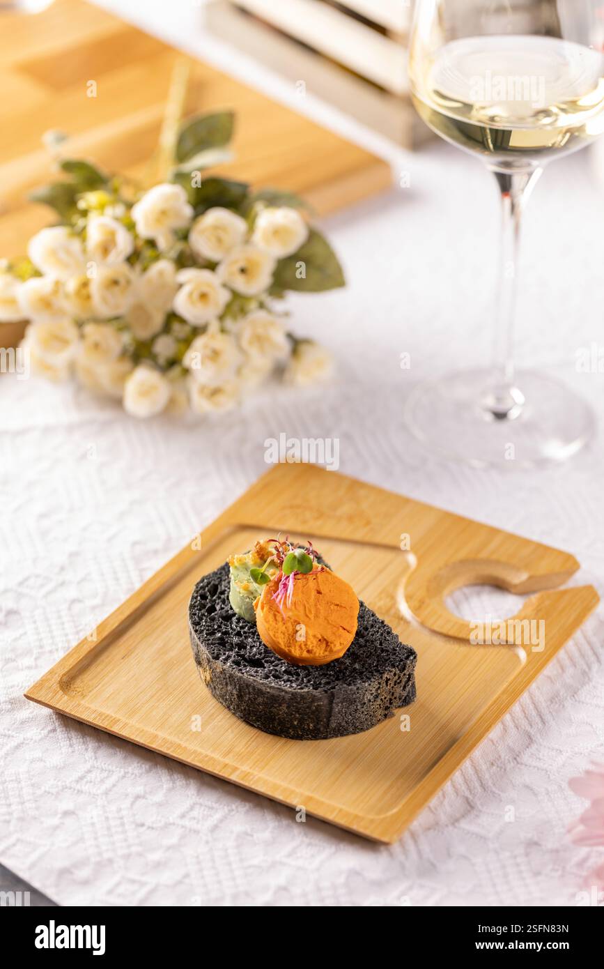 Canapés de pain noir avec tartinades et microgreens servis sur planche de bois avec vin blanc et fleurs Banque D'Images