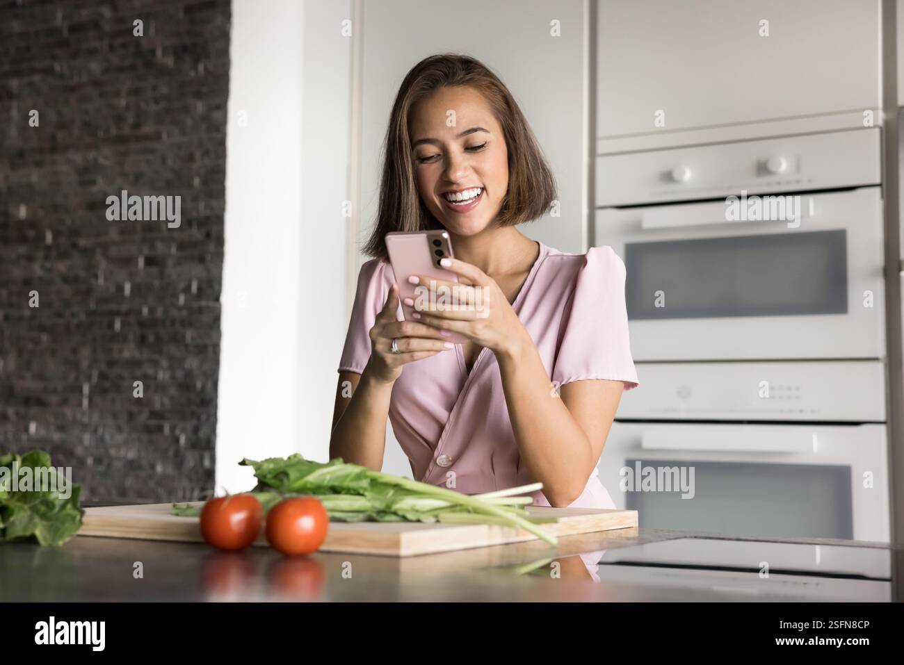 Jolie femme utilisant son smartphone se dresse dans la cuisine Banque D'Images