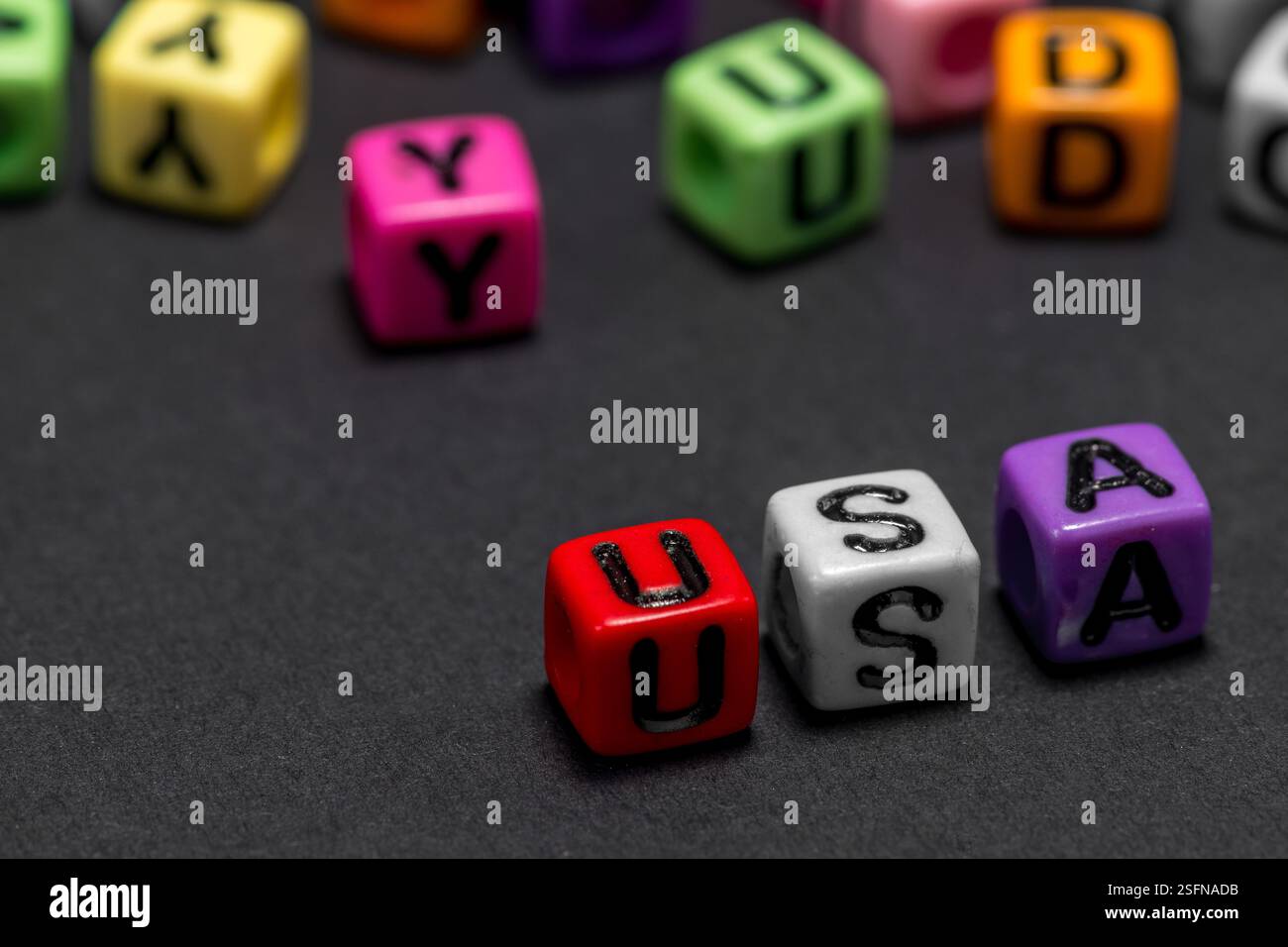 De petits cubes colorés avec des lettres de l'alphabet forment le mot 'USA' (États-Unis d'Amérique) au premier plan, fond noir, espace de copie. Banque D'Images