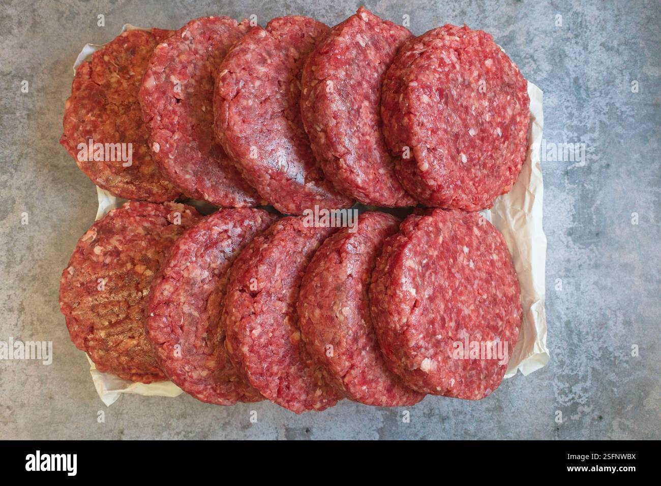 Des burgers de bœuf cru ont été placés sur du papier sur une table en béton. Vue de dessus. Banque D'Images