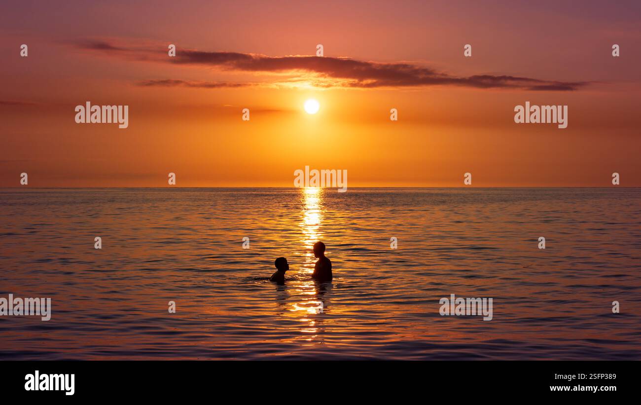 Silhouette de deux personnes se baignant devant un coucher de soleil sur l'océan indien, île Maurice Banque D'Images