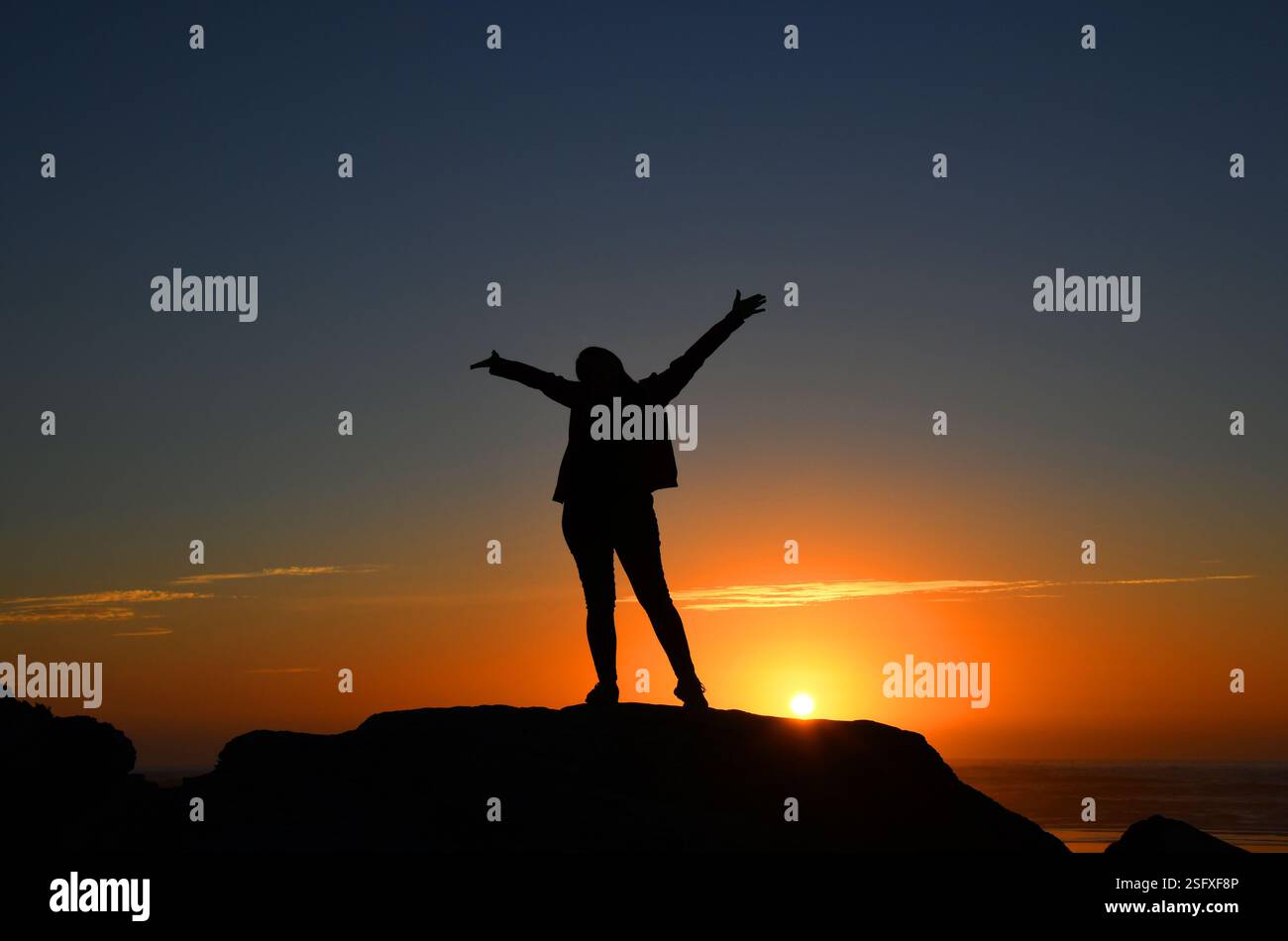 Femme excitée atteint ses bras larges pour embrasser un glorieux coucher de soleil doré sur Bullards Beach State Park. Elle est debout sur un bluff rocheux. Banque D'Images