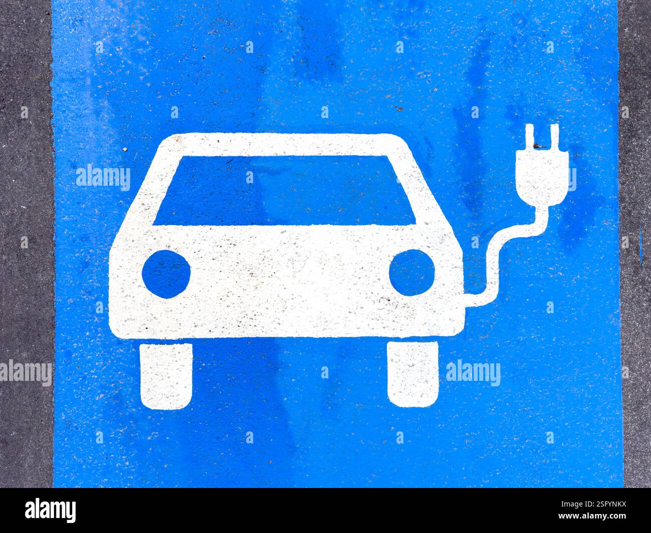 Une image en gros plan montre un symbole peint en blanc d'une voiture électrique branchée sur une station de recharge, située sur un espace de stationnement en asphalte bleu vif. Le Banque D'Images