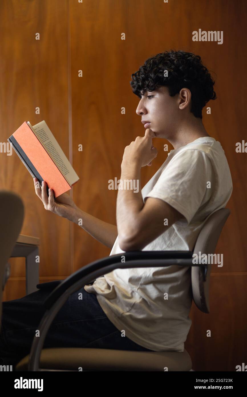 Un jeune lisant réfléchi, posant sa main sur son menton. Idéal pour les thèmes de la pensée profonde, de la lecture, de la contemplation et de l'eng intellectuel Banque D'Images