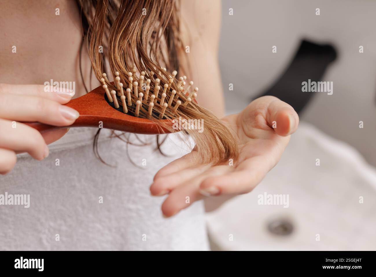 Gros plan d'une femme démêlant les cheveux mouillés avec une brosse en bois. Routine de soins capillaires, beauté et concept d'auto-soin dans un cadre de salle de bain moderne Banque D'Images