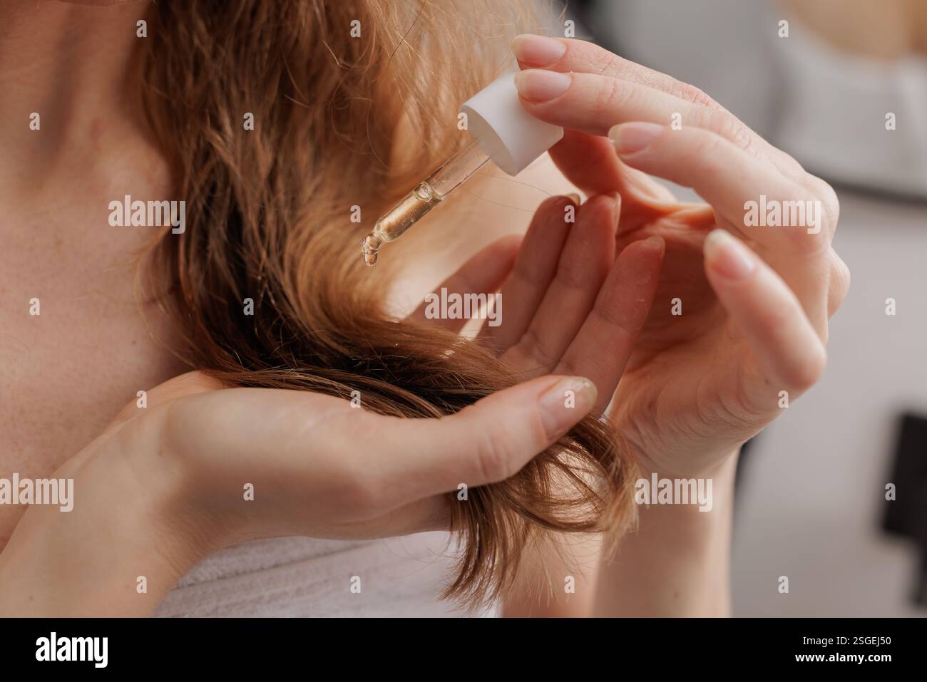 Gros plan d'une femme appliquant de l'huile capillaire ou du sérum avec un compte-gouttes pour nourrir et hydrater les cheveux, améliorant la brillance et favorisant une routine de soins capillaires sains. Banque D'Images