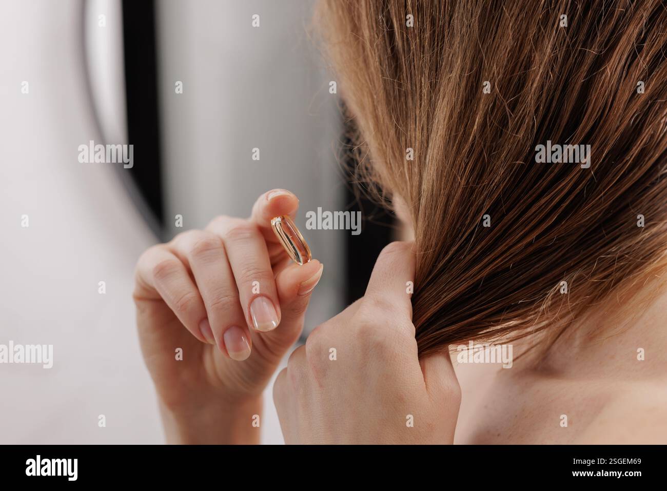 Gros plan d'une femme appliquant une capsule d'huile capillaire pour nourrir et protéger ses cheveux. Concept de routine beauté, soins capillaires et auto-soins Banque D'Images