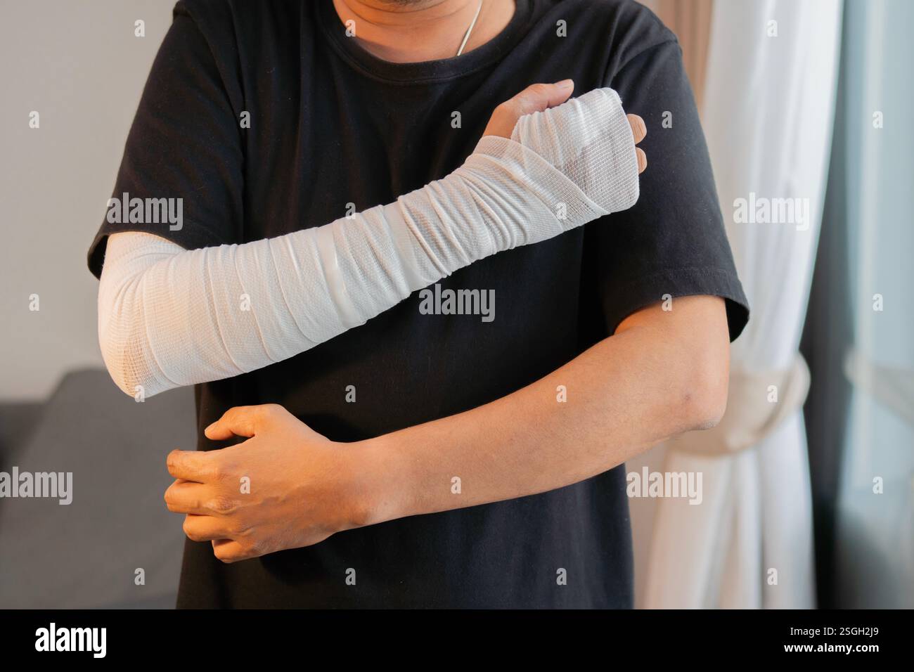 Jeune homme avec un bandage de gaze enroulé autour de ses bras blessés, main et coude à la maison. Concept de premiers soins. Banque D'Images