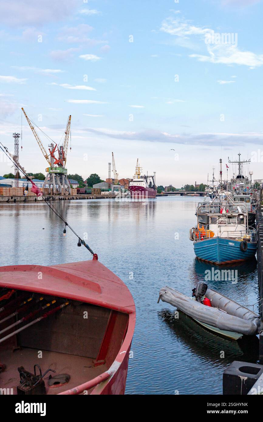 Une vue large d'un port industriel avec divers bateaux, dont un rouge proéminent au premier plan, amarré aux côtés de grues et d'autres ports infras Banque D'Images