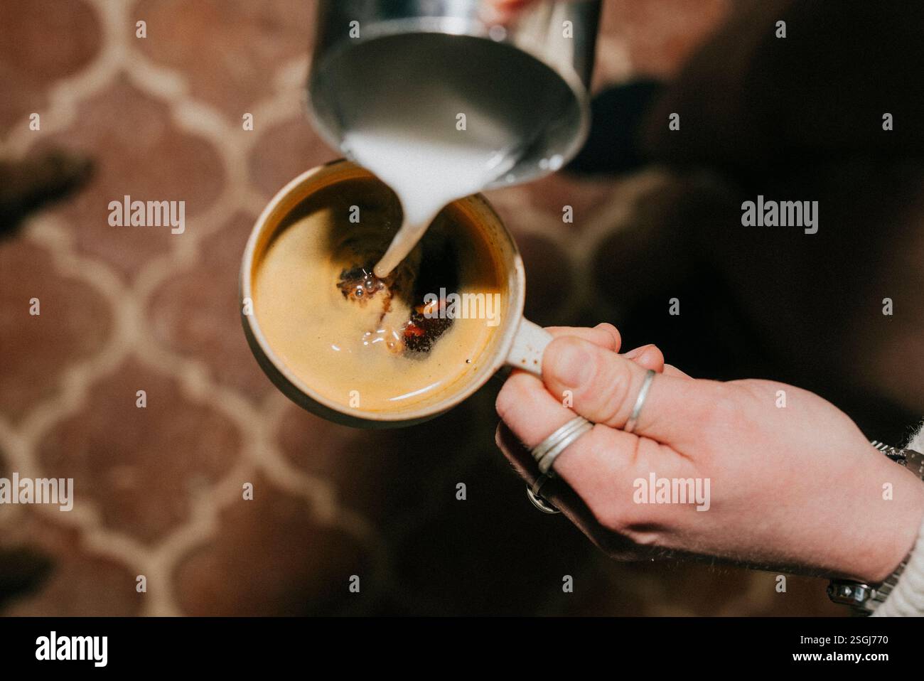 Une personne verse du lait dans une tasse de café. Le café est chaud et le lait est versé lentement Banque D'Images