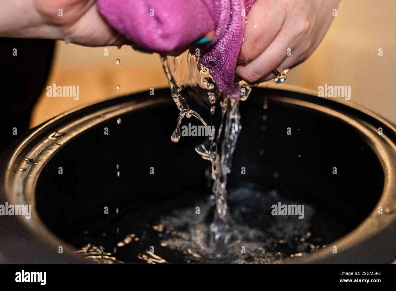 Presser une serviette avec de l'eau s'égouttant dans un bassin noir. Banque D'Images