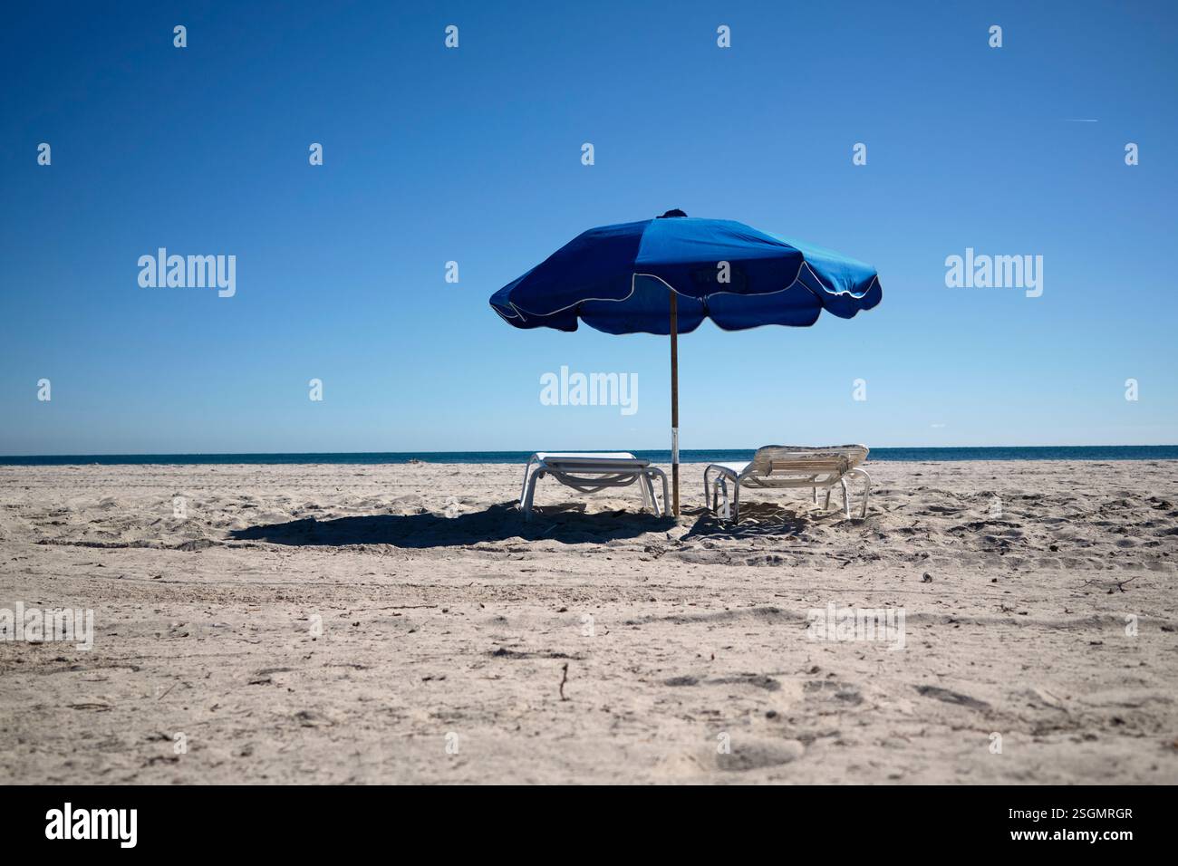 Deux chaises longues et un parasol bleu sur une plage de sable ensoleillée et vide sous un ciel bleu clair, Miami, Floride, États-Unis Banque D'Images