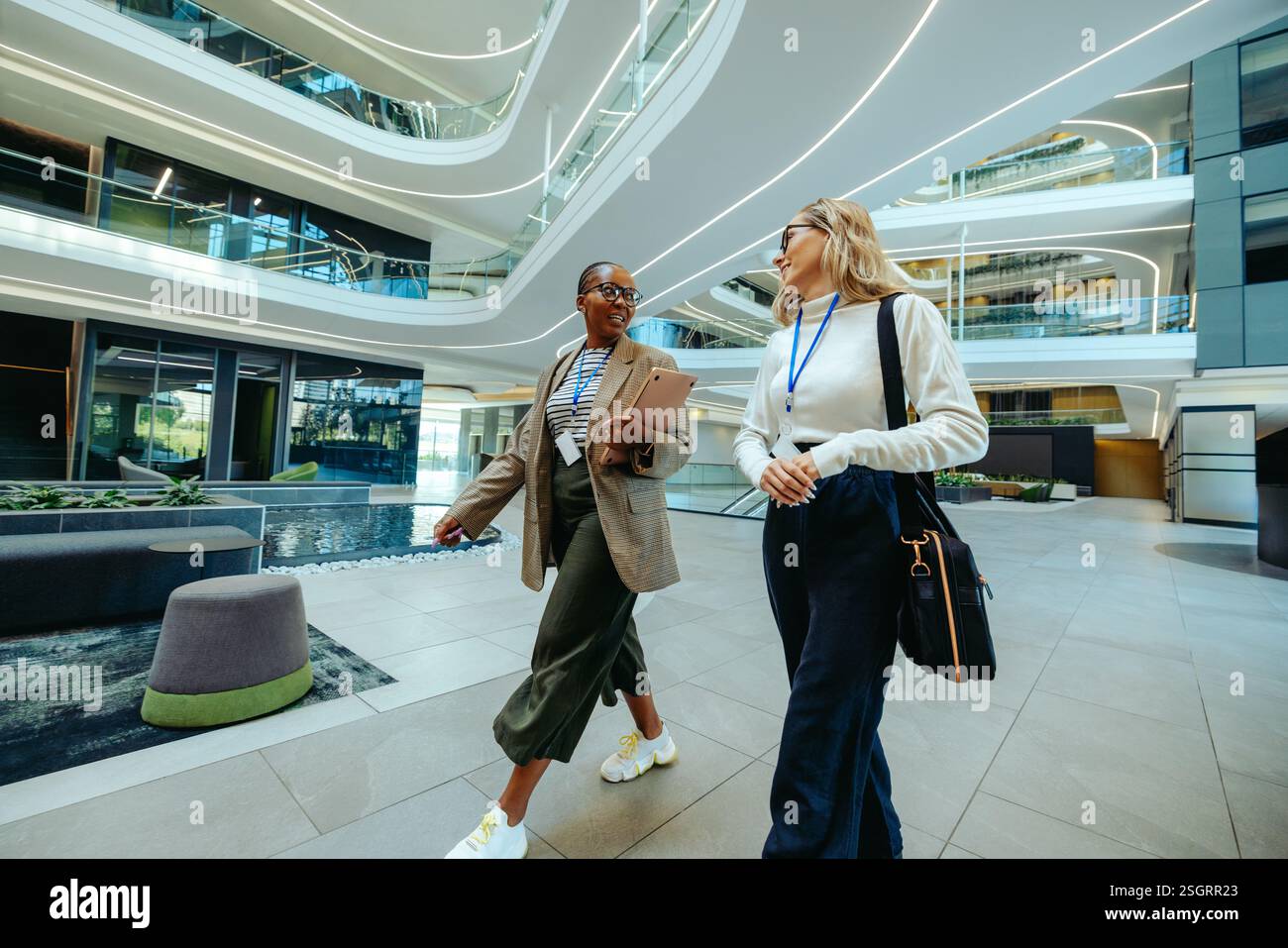 Deux femmes professionnelles marchent dans un environnement de bureau contemporain, s'engageant dans une conversation animée. Travail d'équipe, communication et c moderne Banque D'Images