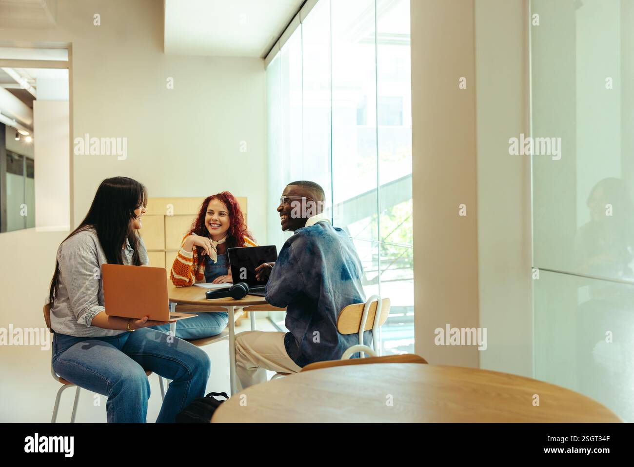 Un groupe d'amis d'université étudiant avec des ordinateurs portables et des livres dans un environnement élégant et lumineux. Ils sont engagés dans l'étude collaborative et l'idée Banque D'Images