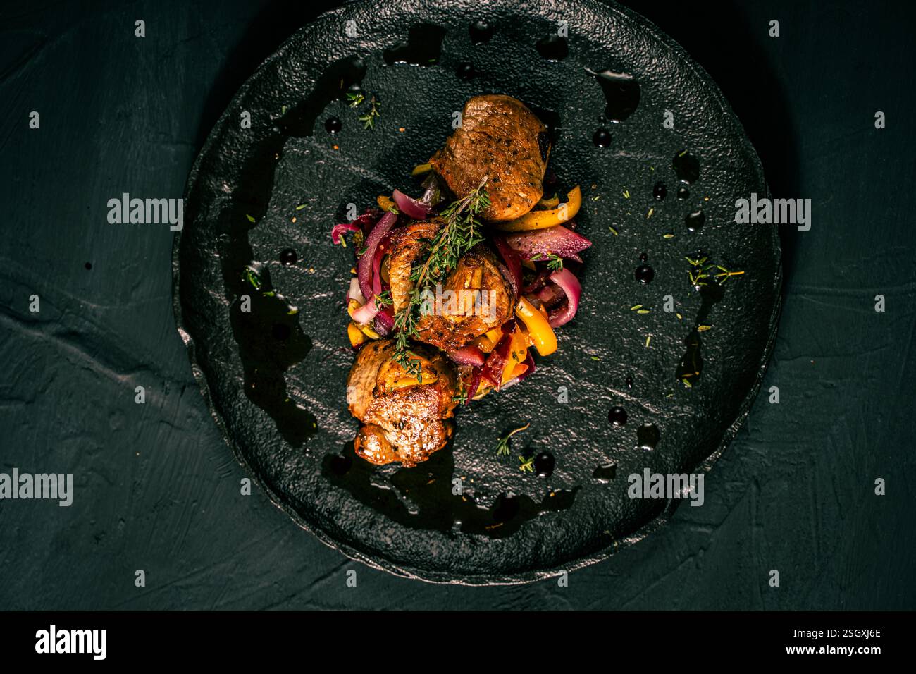 Tranche de filet de porc rôti avec légumes, oignon rose et poivron jaune sur une plaque noire sur fond foncé. Présentation restaurant du d Banque D'Images