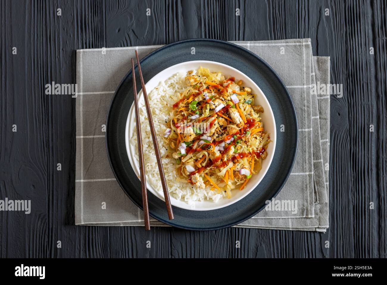 roulé aux œufs de tofu, chou sautés, tofu émietté assaisonné servi dans une sauce sucrée et salée servie sur du riz dans un bol avec des baguettes sur du ta en bois noir Banque D'Images
