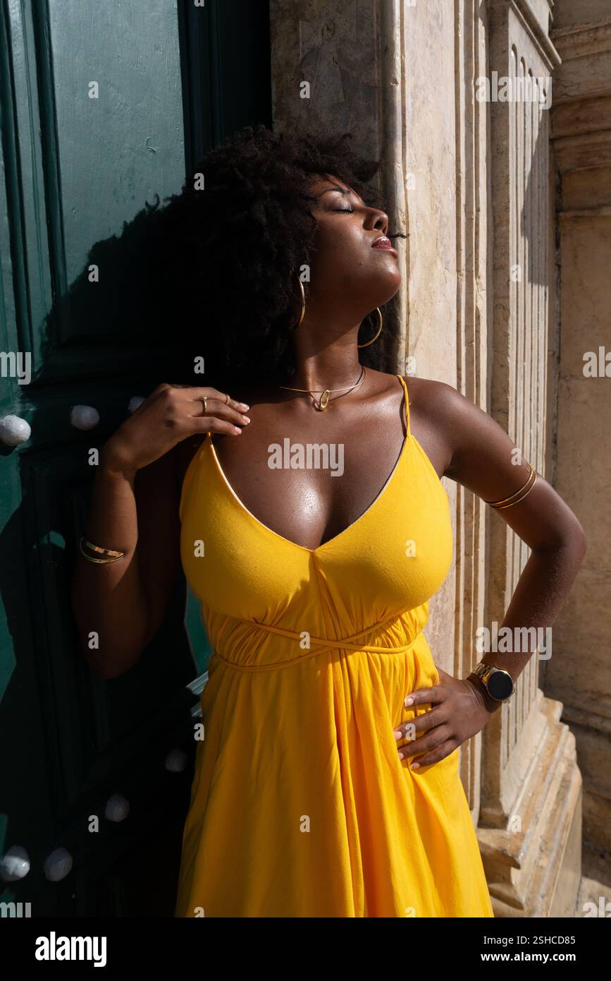 Belle femme noire avec des cheveux de corbeau portant une robe jaune posant pour la photo contre la grande porte verte de l'église. Heureux et souriant Banque D'Images
