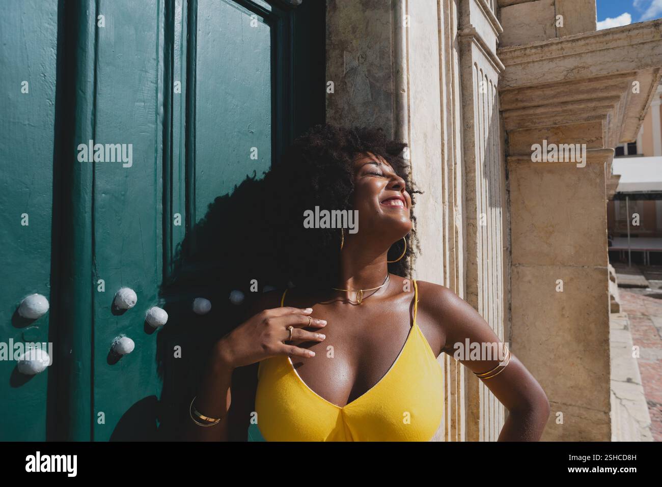Belle femme noire avec des cheveux de corbeau portant une robe jaune posant pour la photo contre la grande porte verte de l'église. Heureux et souriant Banque D'Images