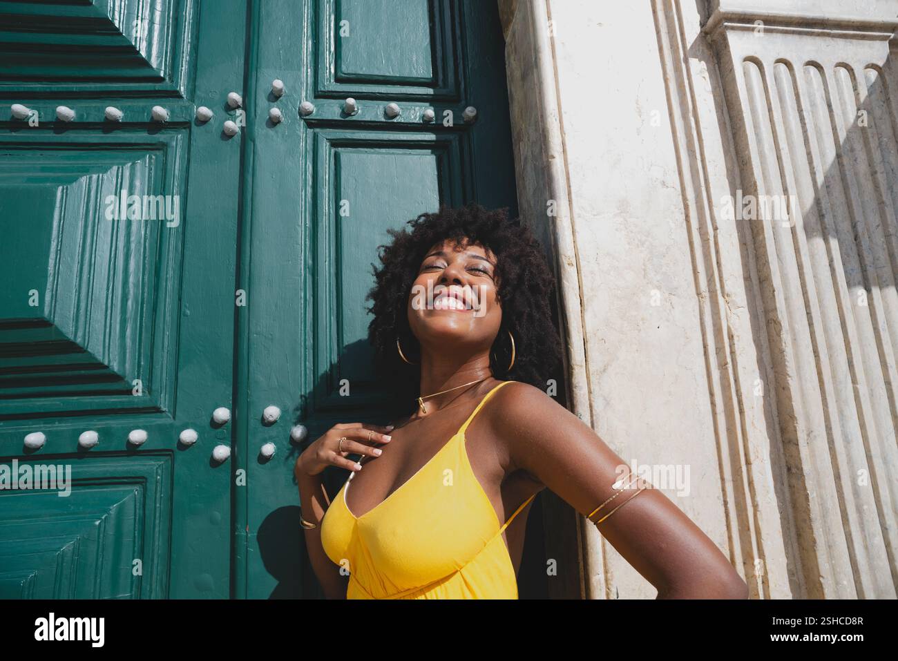 Belle femme noire avec des cheveux de corbeau portant une robe jaune posant pour la photo contre la grande porte verte de l'église. Heureux et souriant Banque D'Images
