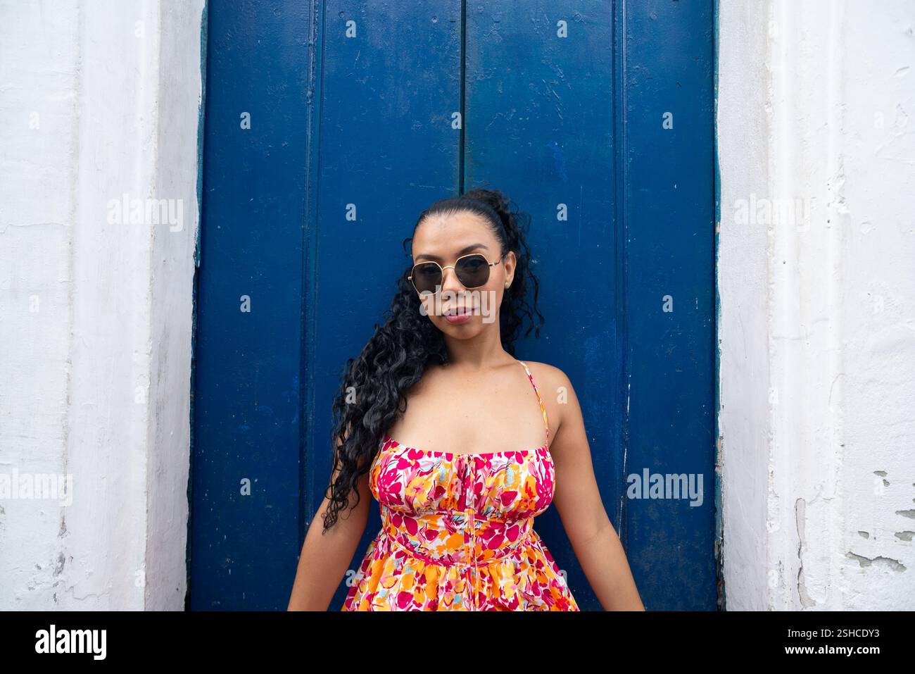 Belle jeune femme caucasienne avec des tresses et une robe colorée assise devant une porte bleue d'une vieille maison posant pour une photo. Personne confiante. B Banque D'Images