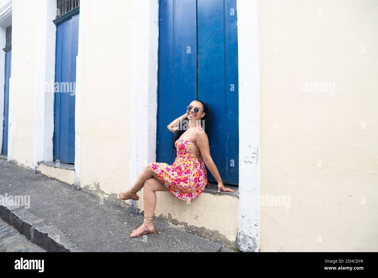 Belle jeune femme caucasienne avec des tresses et une robe colorée assise devant une porte bleue d'une vieille maison posant pour une photo. Personne confiante. B Banque D'Images