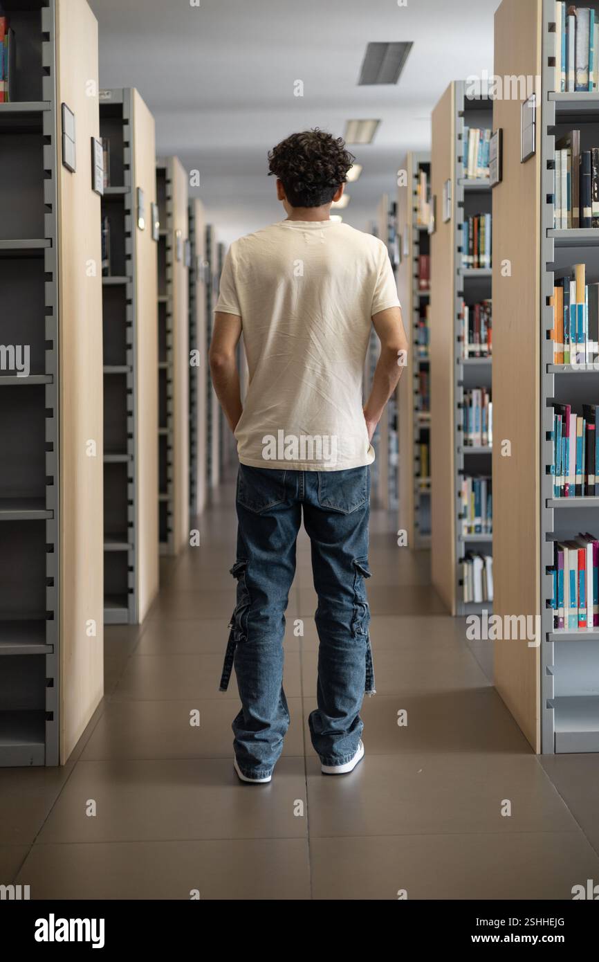 Un jeune étudiant assis dans une bibliothèque, face à face, profondément dans la pensée. Idéal pour des thèmes comme l'étude, la réflexion, l'éducation et la vie académique. Banque D'Images