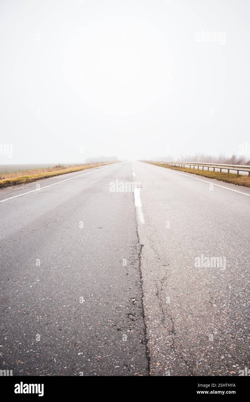 Autoroute vide dans le brouillard. Mauvais temps sur la route. Route le jour brumeux en perspective avec espace de copie. Concept de conditions de conduite. Route brumeuse fantomatique. Banque D'Images