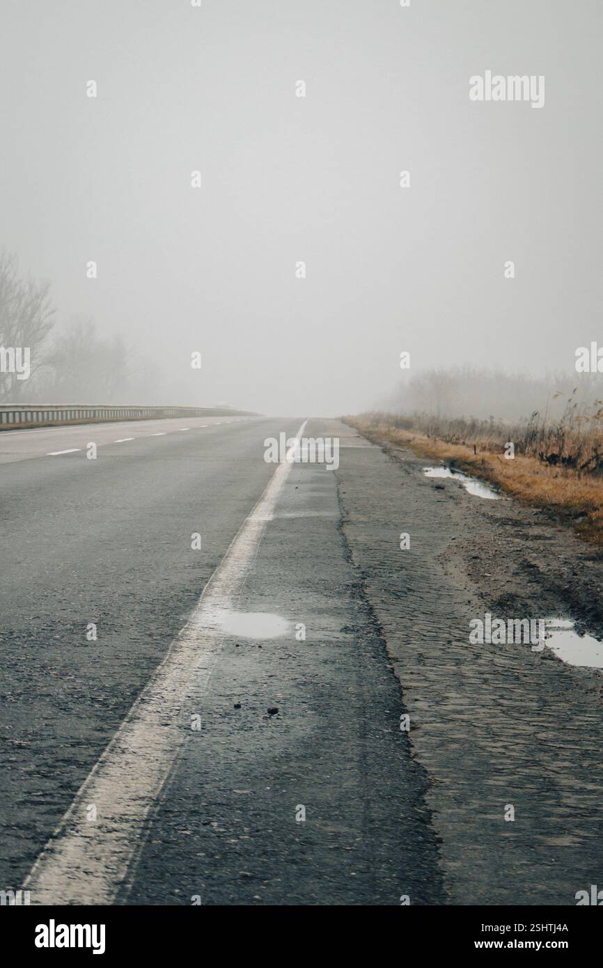 Autoroute vide dans le brouillard. Mauvais temps sur la route. Route le jour brumeux en perspective avec espace de copie. Concept de conditions de conduite. Route brumeuse fantomatique. Banque D'Images