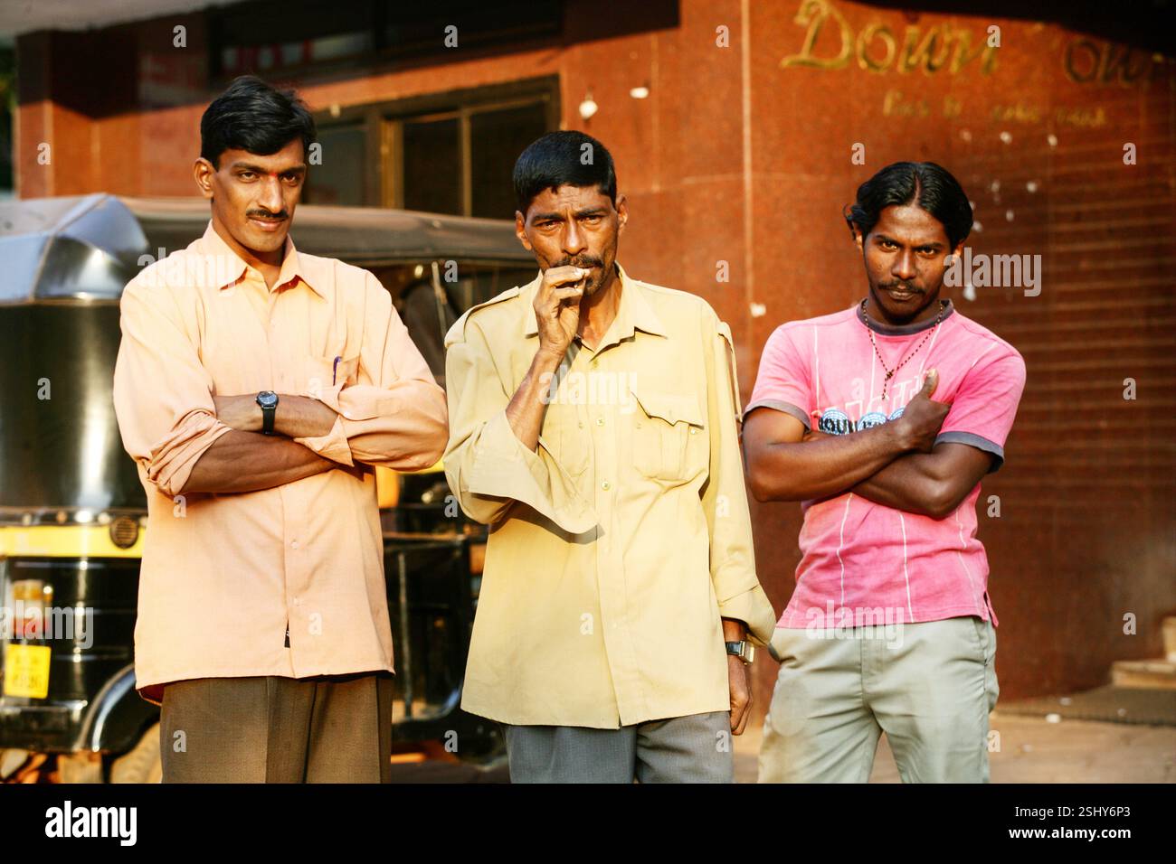 Trois indiens, dont un fumant une cigarette devant une rangée de magasins en Inde. Banque D'Images