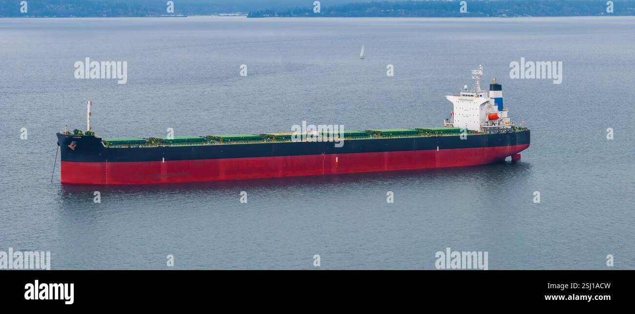 Grand cargo avec coque noire et rouge dans les eaux côtières calmes Banque D'Images