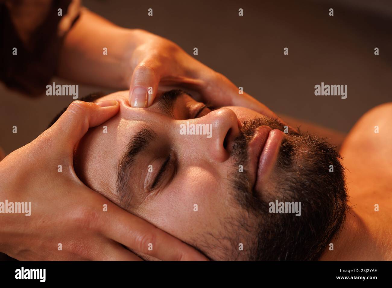 Gros plan d'un homme barbu recevant un massage facial relaxant dans un spa. Un éclairage chaleureux améliore l'atmosphère paisible et thérapeutique de cette auto-CA Banque D'Images