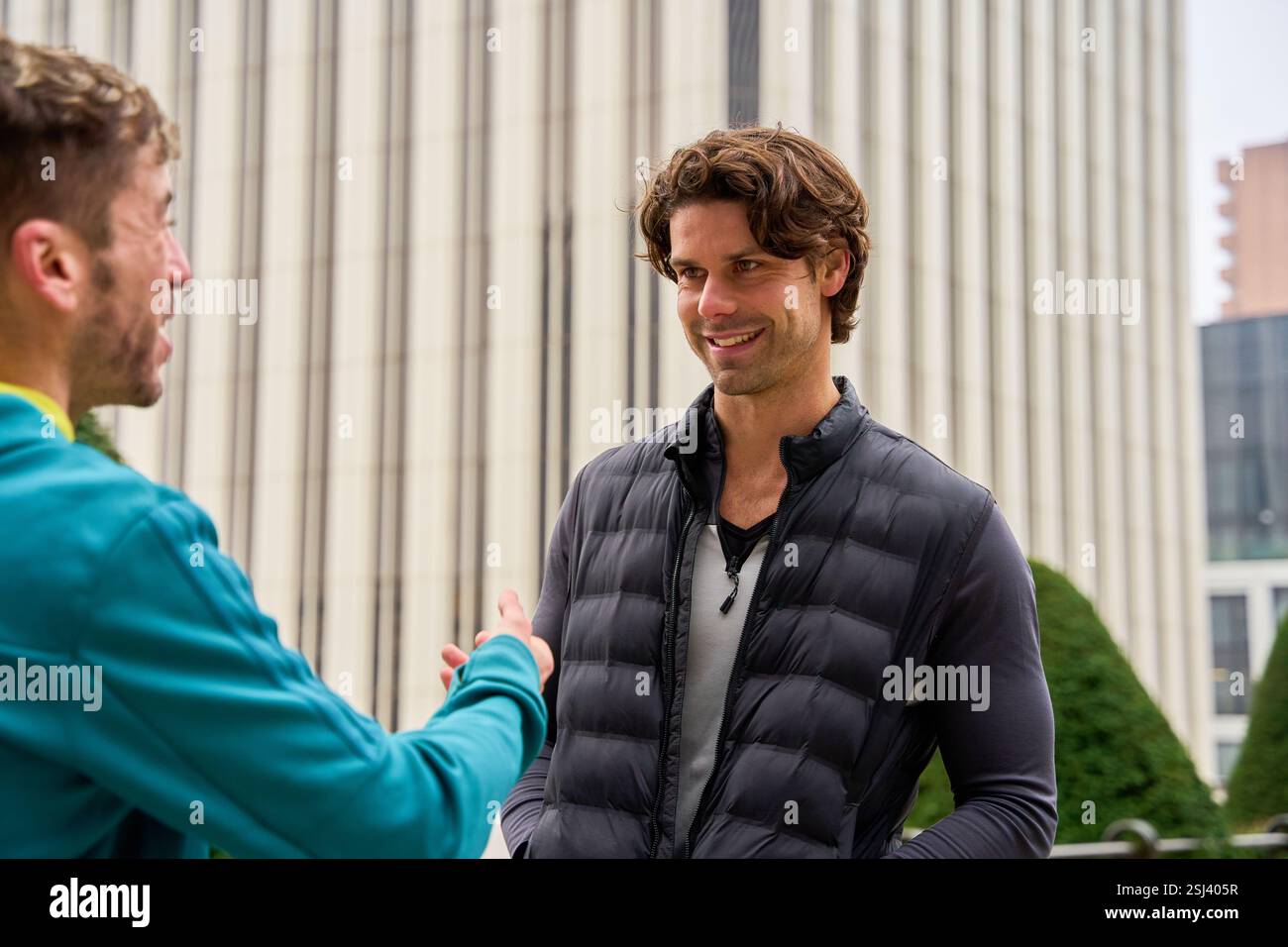 Deux hommes d'affaires ayant une conversation et des gestes dans un cadre urbain moderne, mettant en valeur la communication et la collaboration professionnelles Banque D'Images