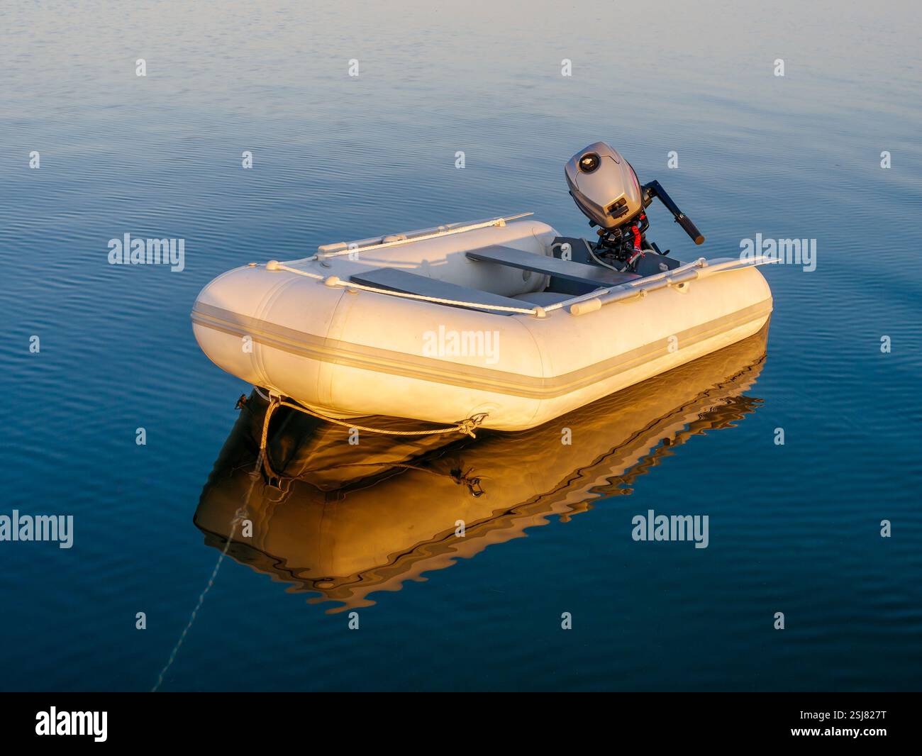Petit dinghy gonflable servant de yacht tendon avec moteur hors-bord amarré à côté d'un yacht sur une mer calme et vitreuse au coucher du soleil Banque D'Images