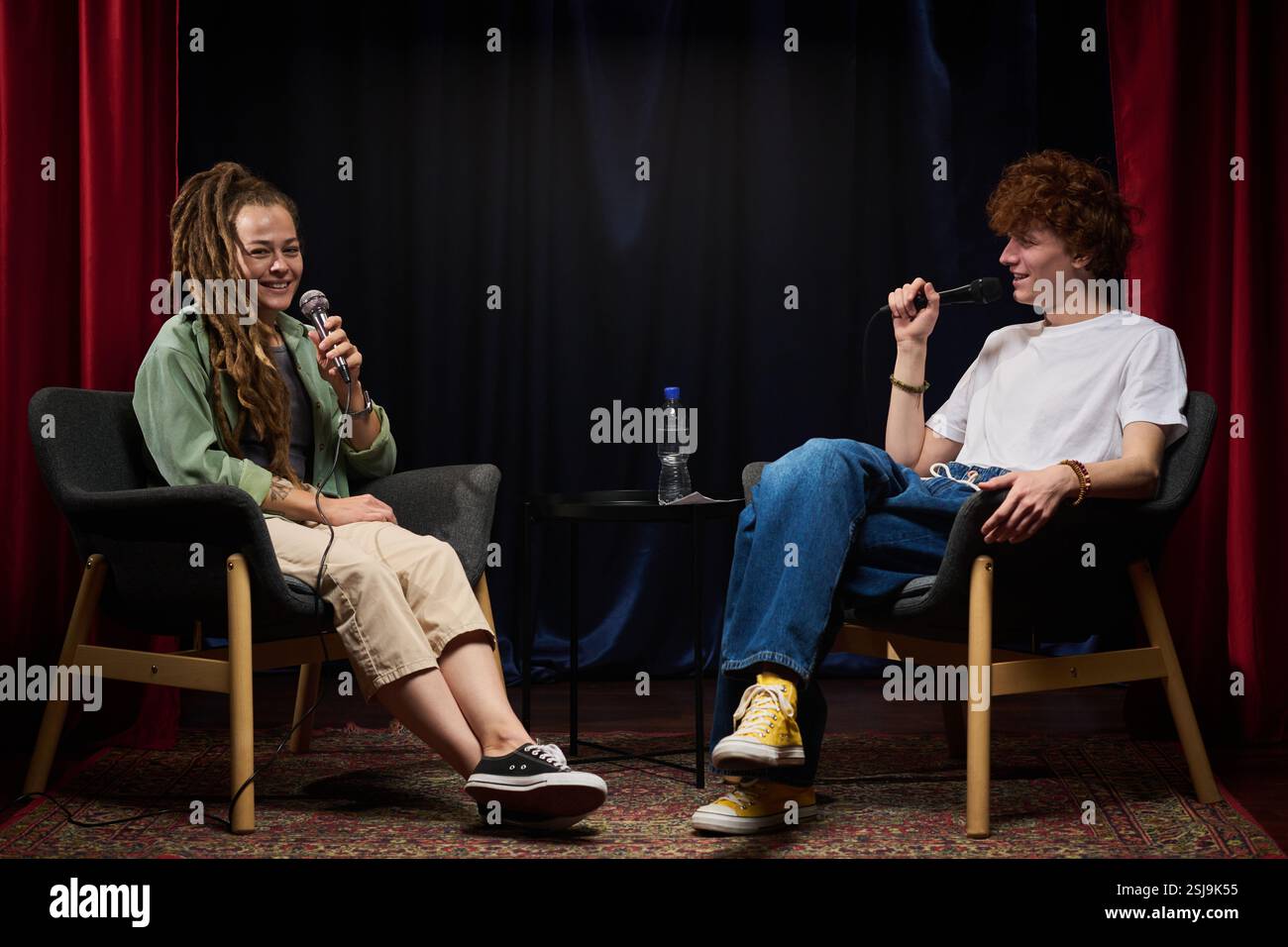 Deux personnes assises sur des chaises tout en enregistrant un podcast avec des microphones à la main, semblant partager une conversation agréable. Divers participants échangent des gestes allégés Banque D'Images