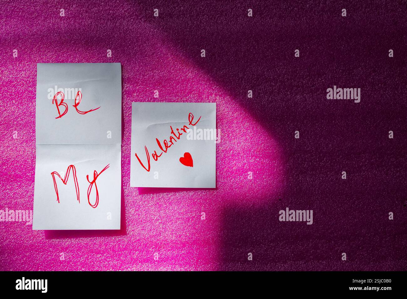 Une note collante sur le thème de l'amour avec « Be My Valentine » écrit dessus, présentée sur une surface rose. Banque D'Images