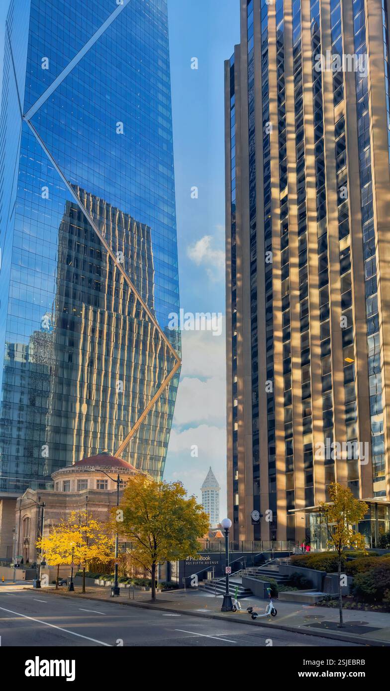 L'image capture une rue de Seattle bordée de hauts gratte-ciel, leurs façades en verre reflétant le ciel bleu et les bâtiments environnants. Banque D'Images