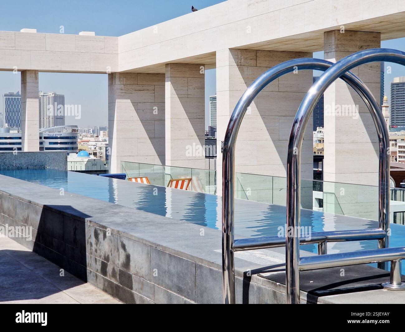 Dubai, Emirates - 2024-05-26 : Une luxueuse piscine sur le toit avec une échelle métallique élégante donnant sur un horizon urbain moderne. Banque D'Images