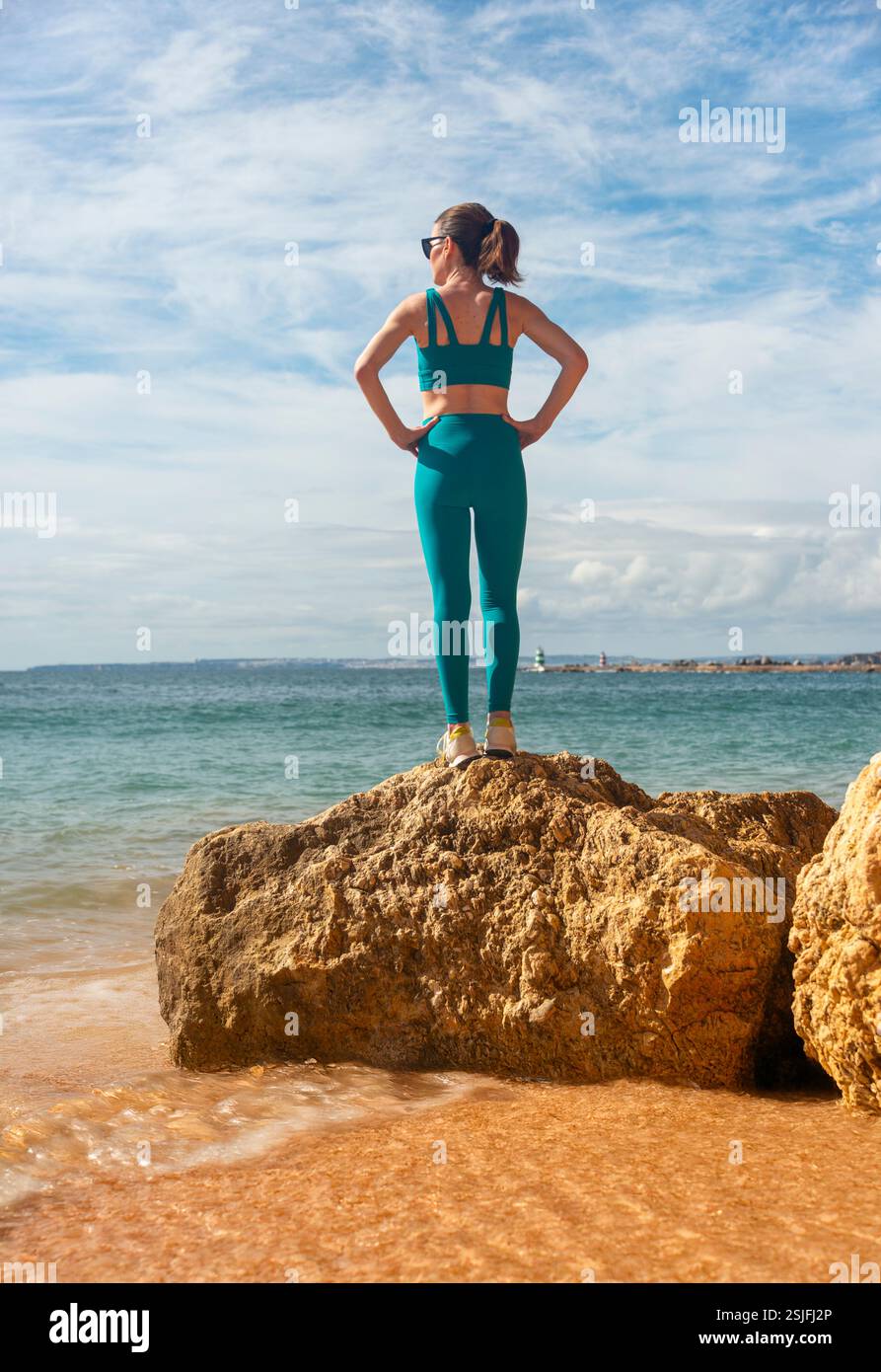 femme sportive debout sur un rocher au bord de la mer avec les mains sur ses hanches Banque D'Images femme sportive debout sur un rocher au bord de la mer avec les mains sur ses hanches Banque D'Images